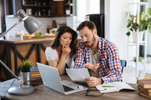 frustrated couple comparing furnace repair and replacement costs using their laptop