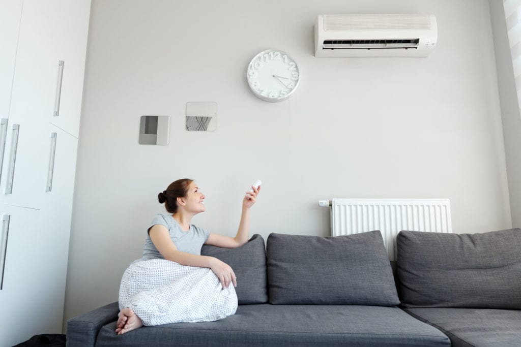 Woman sitting in a sofa and adjusting the heating system in her home by using a remote control