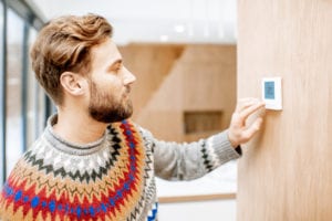 Man adjusting the temperature of his thermostat at home during winter.