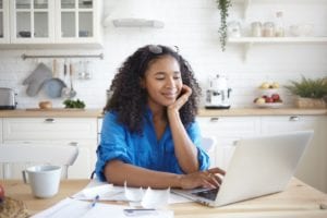 woman sitting at her kitchen table with a laptop looking at ease with her home environment