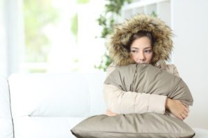 woman sitting on couch in a parka from the room being cold